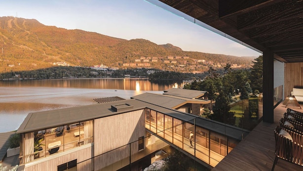 Ein modernes Gebäude mit Glasfassade, Blick auf einen See und Berge.