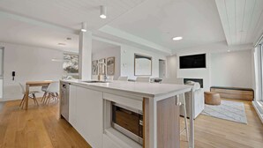Eine moderne Küche mit Kochinsel, Essbereich mit Stühlen und Wohnbereich mit Sofa und Fernseher.