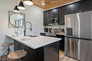 A modern kitchen with a central island, stainless steel appliances, and a wooden ceiling. - Heated Indoor Pool, Luxury Cabin, Near Dollywood (Sevierville)