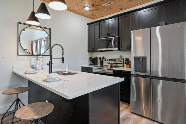 A modern kitchen with a central island, stainless steel appliances, and a wooden ceiling.