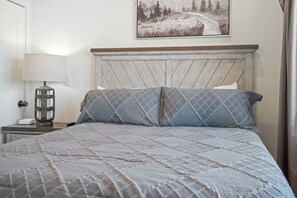 A neatly made bed with a quilted cover, a bedside lamp, and a wall-mounted painting. - Luxe Cabin W Indoor Pool・Spacious Cabin, Sleeps 10 (Sevierville)