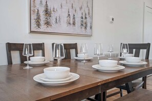 A dining table set with white plates, bowls, and wine glasses, with a painting of trees on the wall behind. - Heated Indoor Pool, Luxury Cabin, Near Dollywood (Sevierville)
