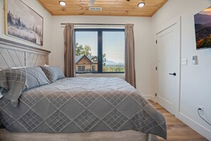 A bedroom with a large bed, a wooden ceiling, a window with curtains, and a painting on the wall. - Heated Indoor Pool, Luxury Cabin, Near Dollywood (Sevierville)