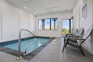 An indoor pool area with a metal pool ladder, lounge chairs, and a view of trees through the windows. - Luxe Cabin W Indoor Pool・Spacious Cabin, Sleeps 10 (Sevierville)