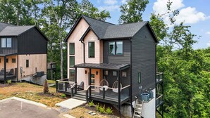 A modern two-story cabin with a balcony, a deck, and a small outdoor seating area.