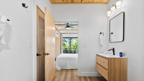 A modern bathroom with a wooden vanity, a ceiling fan, and a view of a balcony.