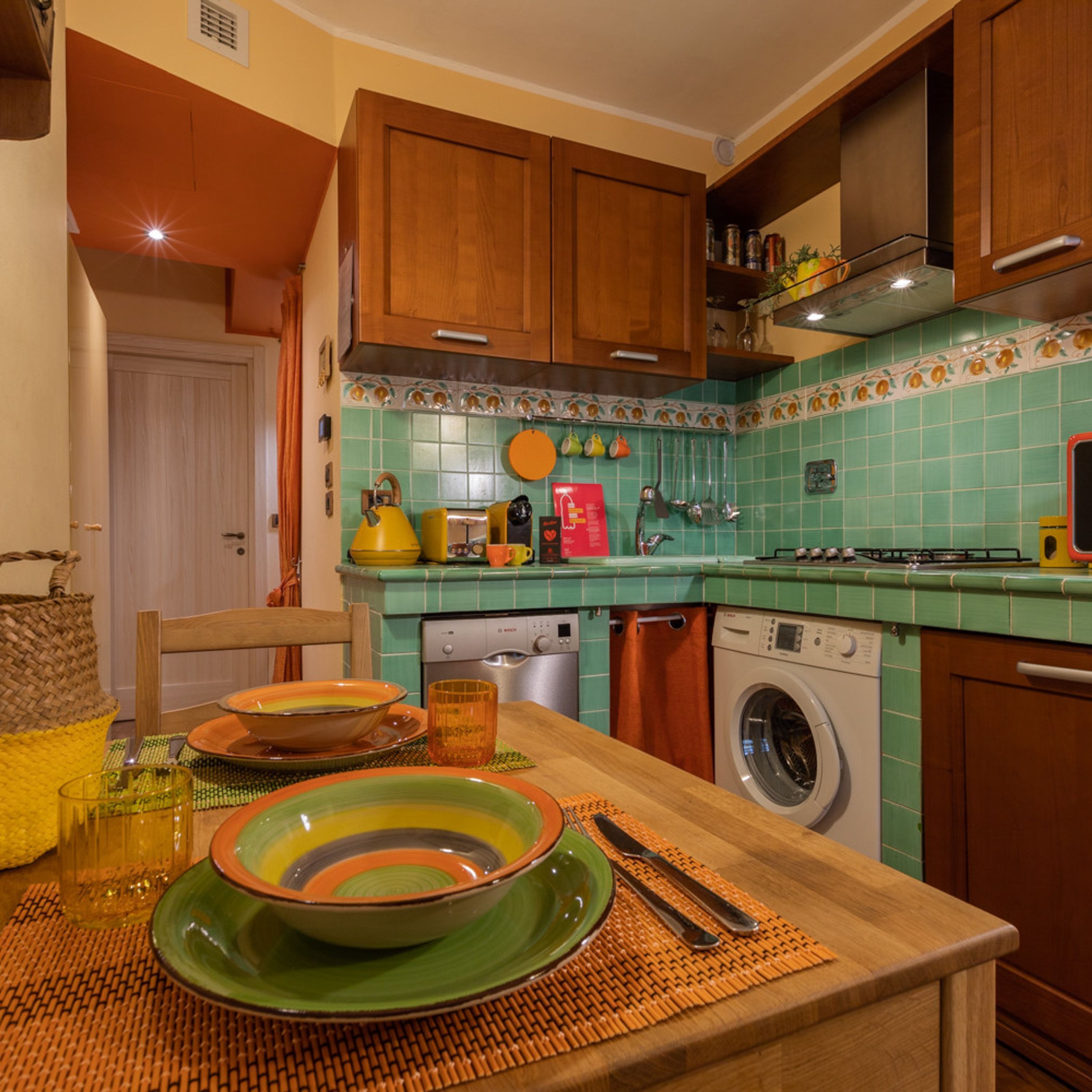 Una cocina con armarios de madera, lavadora y comedor con una mesa para dos.