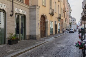 A cobblestone street with a building labeled "OSTERIA" featuring a large arched doorway and a small balcony with plants.