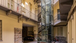 A spacious courtyard with a glass elevator shaft, potted plants, and a bicycle. - I Vicini del Re by Wonderful Italy (Turin)