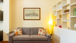 A living room with a grey sofa, a framed picture on the wall, and a white shelving unit with decorative items. - Casa Vacanze Nostos Alabardieri by Napoliapartments (Naples)