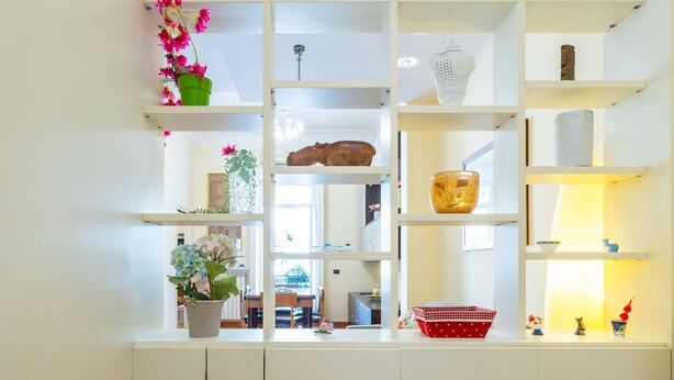 A white interior with a built-in shelving unit displaying various decorative items and a view into a dining area. - Casa Vacanze Nostos Alabardieri by Napoliapartments (Naples)