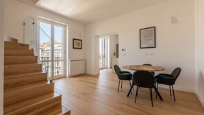 A spacious room with a wooden staircase, a dining area with a round table and chairs, and a view through large windows. - Oretea Apartment With Terrace by Wonderful Italy (Palermo)