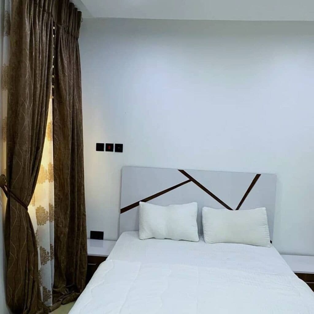 A bedroom with a white bed, brown curtains, and a modern headboard.