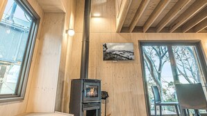 Moderni sisustus, jossa on puukamiina, suuret ikkunat ja korkea kattokorkeus.