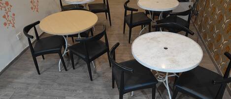 A room with four round tables and six black chairs. The walls have floral wallpaper, and the floor is wooden.