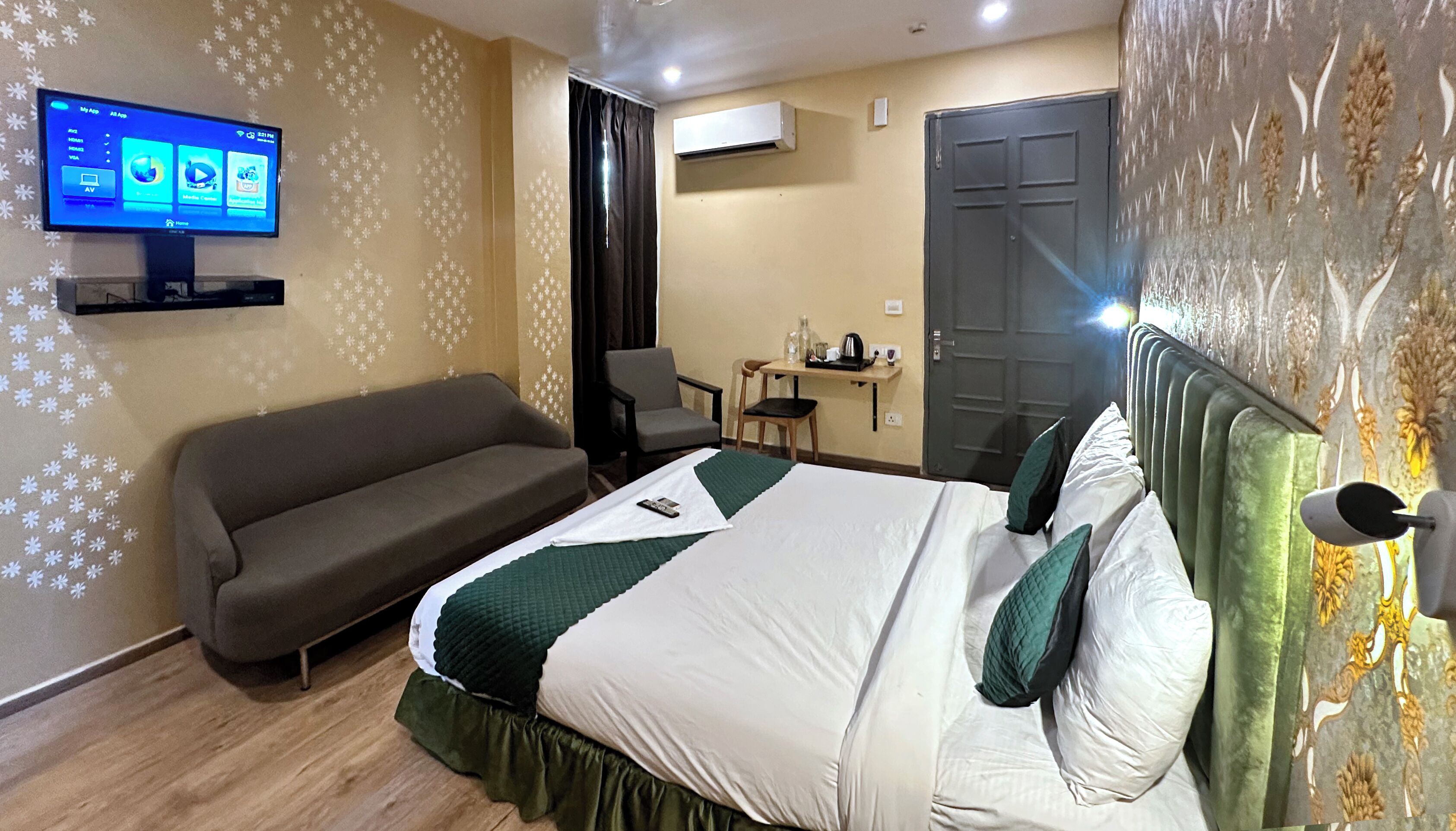 Una habitación de hotel con cama, sofá, televisor, escritorio y aire acondicionado.
