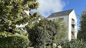 Un camí que porta a un edifici blanc amb balcons, envoltat de vegetació abundant i plantes florides.