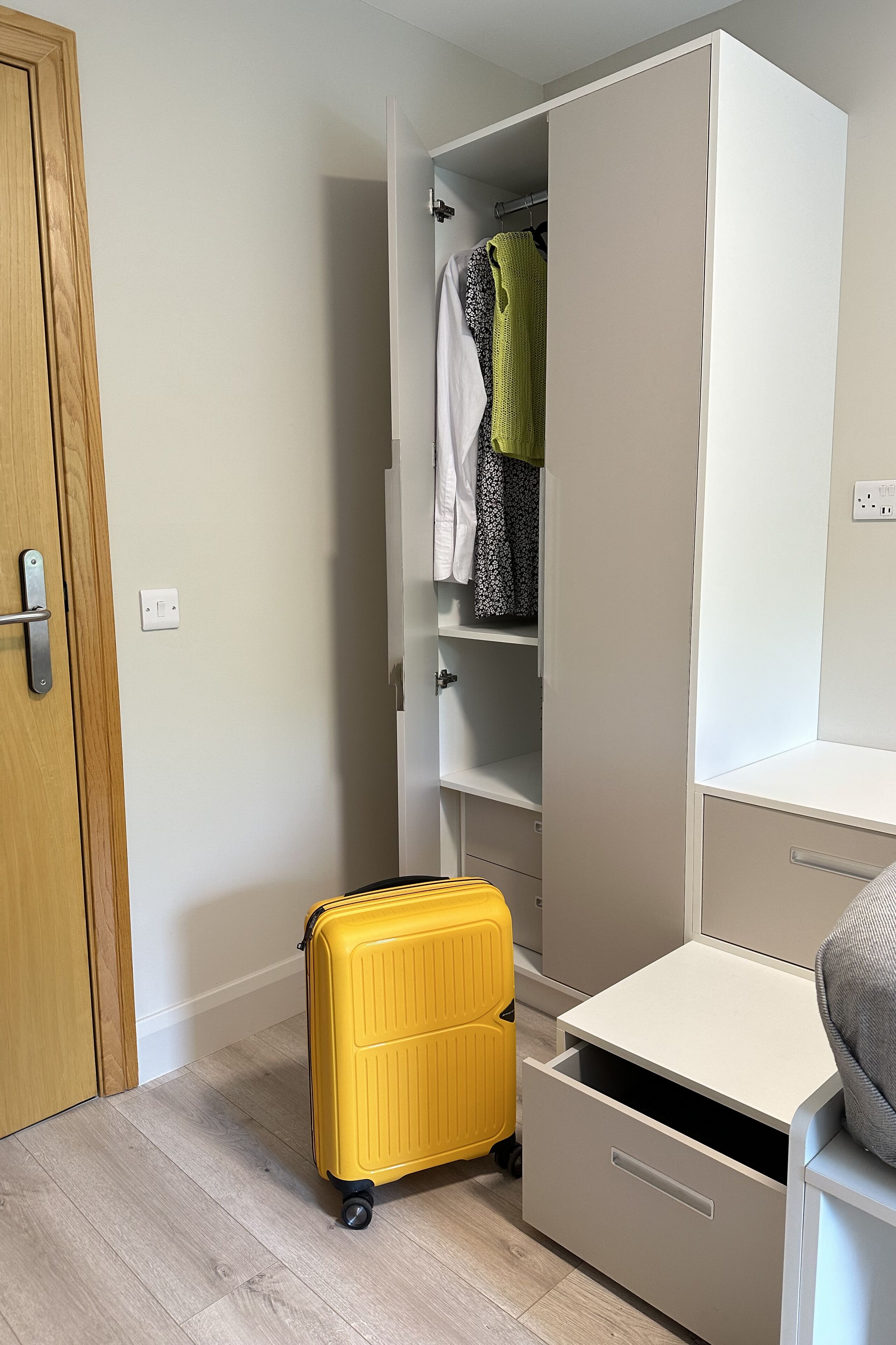 Una habitación pequeña con un armario, un escritorio y una maleta amarilla.