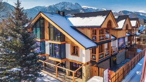 A wooden chalet with a balcony, large windows, and a view of snow-covered mountains. - Mountain Shelter Apartments (Zakopane)