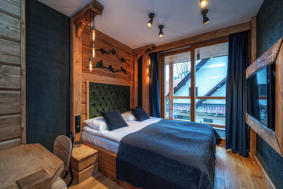 A wooden cabin-style bedroom with a large bed, a desk, and a view of the outside.
