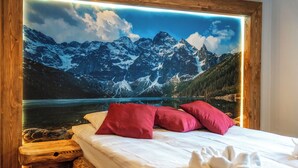 A bed with white bedding and red pillows, a wooden headboard, and a scenic mountain landscape mural above it. - Mountain Shelter Apartments (Zakopane)
