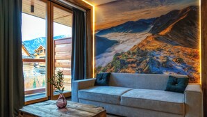 A modern living room with a large window, a wooden coffee table, a grey sofa, and a mountain landscape mural on the wall. - Mountain Shelter Apartments (Zakopane)