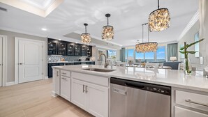 Une cuisine moderne dotée d’un grand îlot central, d’appareils électroménagers en acier inoxydable et de lustres décoratifs.