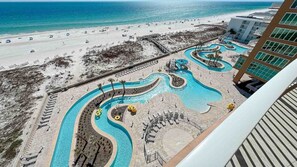 A resort with a beach, a pool area with winding water features, and a view of the ocean. - New Complex! BeachFront! Lazy River/Slide!! Parking Level!! (Orange Beach)