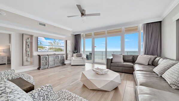 A spacious living room with a large window overlooking the ocean, a ceiling fan, and a modern fireplace. - New Complex!  BeachFront!  Lazy River/Slide!!  Parking Level!! (Orange Beach)