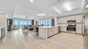 A spacious kitchen with a central island, modern appliances, and large windows offering a view of the ocean. - New Complex!  BeachFront!  Lazy River/Slide!!  Parking Level!! (Orange Beach)