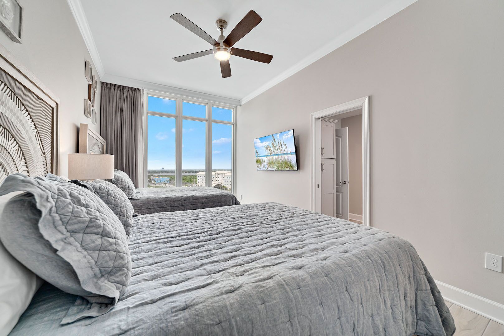 A bedroom with a large bed, a ceiling fan, a TV, and a view of the outdoors.