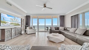 A spacious living room with a large TV, a fireplace, a balcony with a view of the ocean, and a ceiling fan. - New Complex!  BeachFront!  Lazy River/Slide!!  Parking Level!! (Orange Beach)
