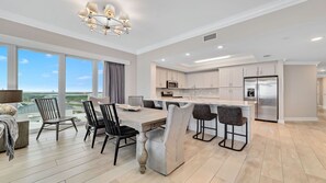 A modern kitchen with a central island, bar stools, and a dining area with a view. - New Complex!  BeachFront!  Lazy River/Slide!!  Parking Level!! (Orange Beach)