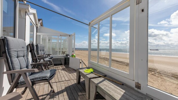 A deck with a view of the beach, a chair, a table, and a bench.