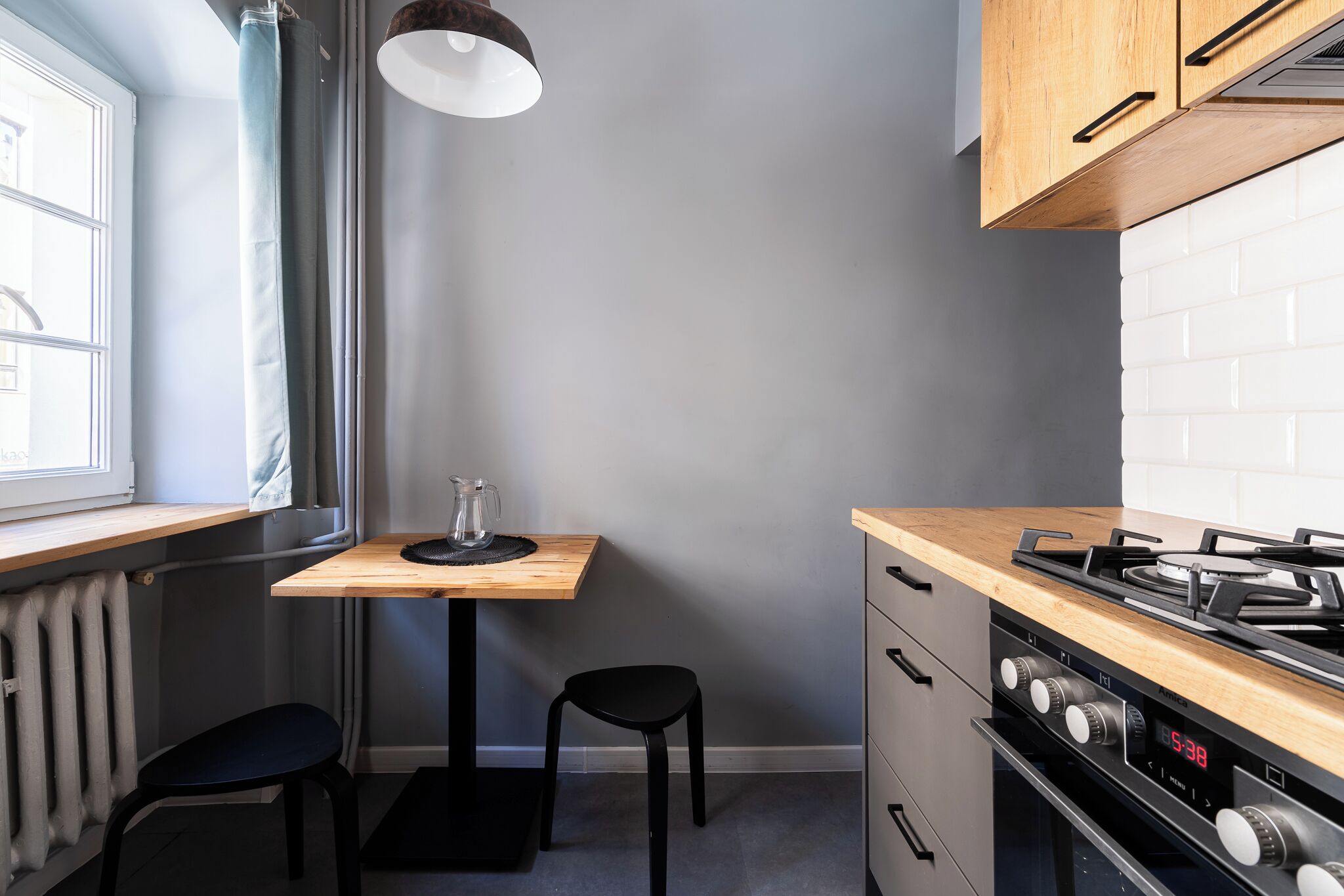 Una cocina compacta con encimera de madera, estufa a gas, una pequeña mesa con una silla y una ventana con cortinas.