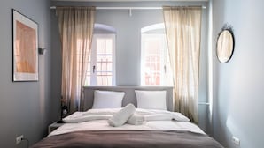 A neatly made bed with white linens and a rolled towel, a framed artwork on the wall, and a round mirror. - RentPlanet - Apartament Malarska (Wroclaw)