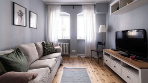 A modern living room with a sofa, TV, and wooden flooring. - RentPlanet - Apartament Malarska (Wroclaw)