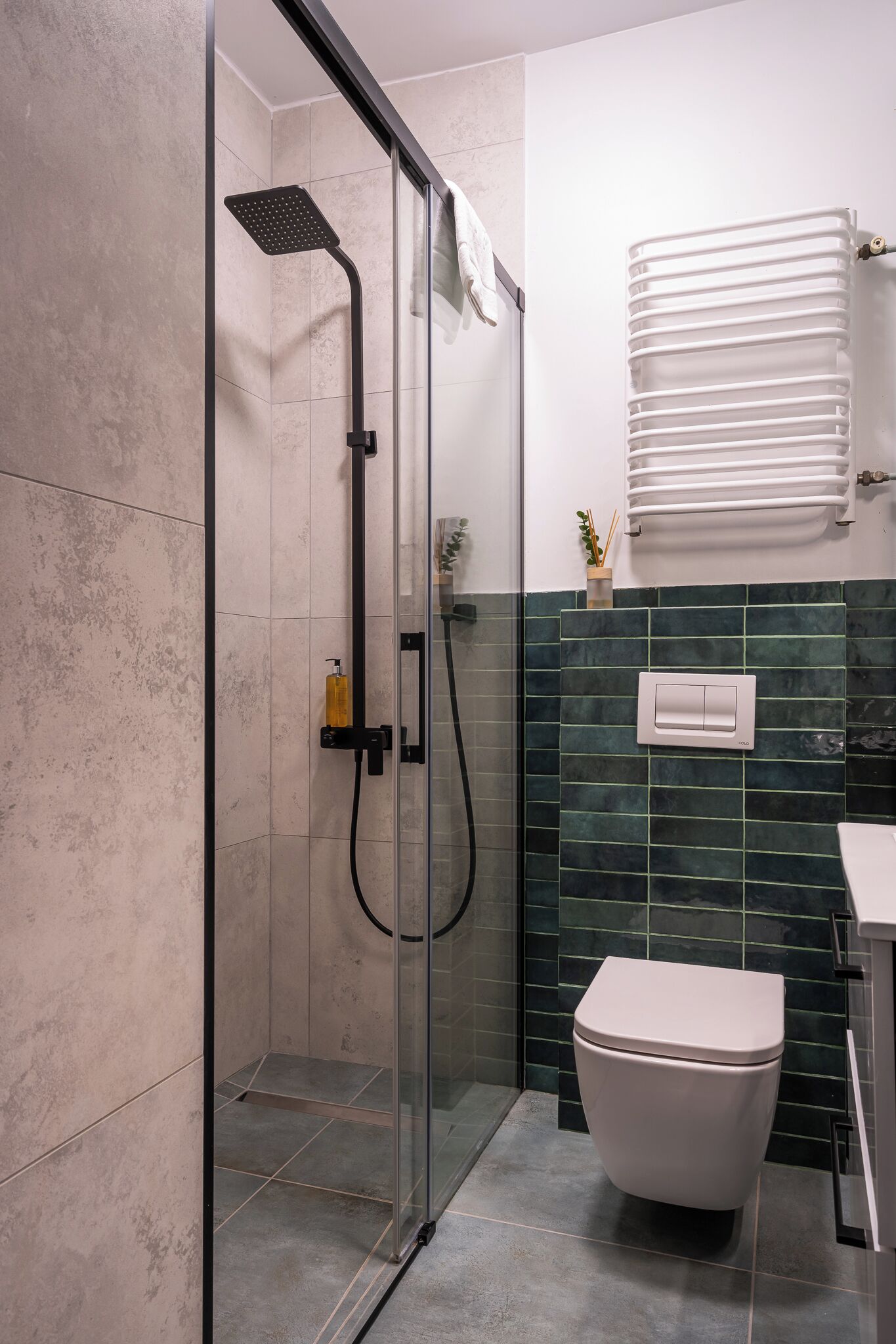 A modern bathroom with a glass-enclosed shower, a white toilet, and a green-tiled wall.