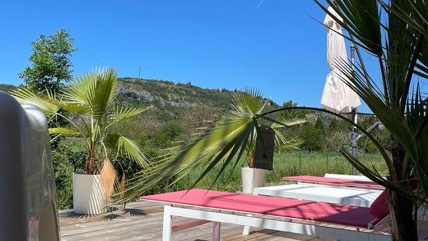 A wooden deck with a red lounge chair and a white table, surrounded by potted plants and a white umbrella. - "vers L'horizon" - Maison de Vacances à 800m de Cajarc Dans le Lot (Salvagnac-Cajarc)
