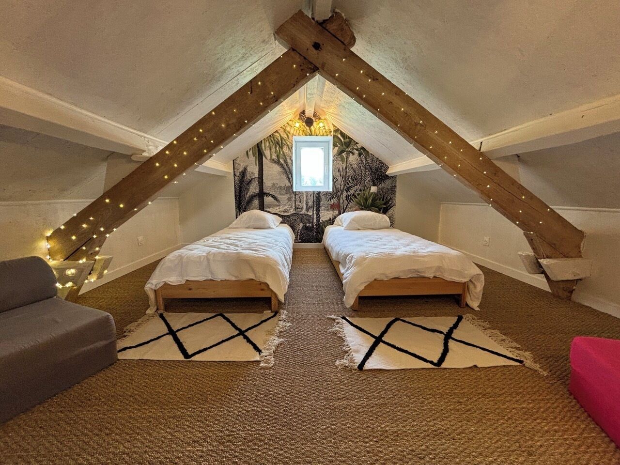 Une chambre mansardée chaleureuse avec deux lits, un canapé gris et un fauteuil rouge.