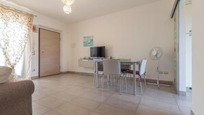 Ein Zimmer mit Esstisch, Stühlen, Fernseher und Ventilator.