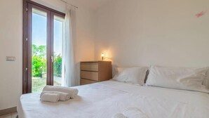 Ein Schlafzimmer mit Bett, Nachttisch, Lampe und Blick auf einen Balkon.