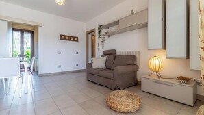 Ein modernes Wohnzimmer mit einer Couch, einem Beistelltisch und einer Lampe. Auf dem Boden steht ein Korb und eine Tür führt in einen anderen Raum.