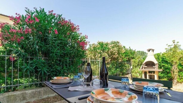 Ein Essbereich im Freien mit einem Tisch für vier Personen, umgeben von üppiger Vegetation und einem Grill im Hintergrund.