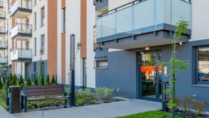 Un immeuble d’appartements moderne, doté d’une entrée en verre, d’un banc et d’un petit espace jardin.