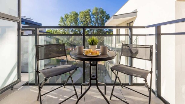 Un balcon moderne avec une paroi en verre, deux chaises, une petite table ronde et un pot de fleurs.
