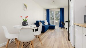 Un salon moderne comprenant une table à manger, des chaises blanches, un canapé bleu et un coin cuisine avec des meubles blancs.