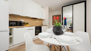 Une cuisine moderne avec des meubles blancs, un plan de travail en bois et un coin repas agrémenté d’une table ronde préparée pour deux personnes.