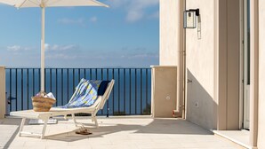 A balcony with a white umbrella, a lounge chair, and a wicker basket.