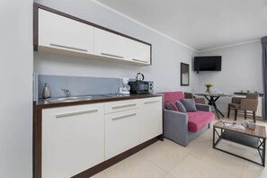 A compact living space with a kitchenette, a sofa, a coffee table, and a flat-screen TV.